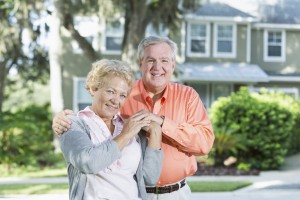 Senior couple standing in front of house.